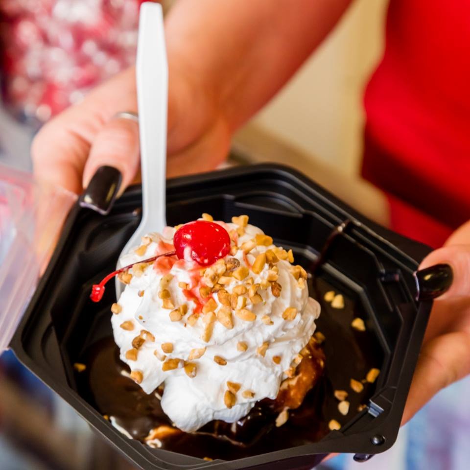 A hot fudge sundae with whipped cream, chopped nuts and a cherry, held in a black dish