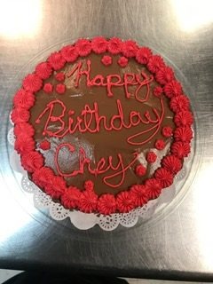 A chocolate frosted cake ringed with red piped rosettes, with a birthday message written on top