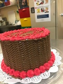 A tall chocolate cake with basketweave frosting on the sides and pink rosettes around the base