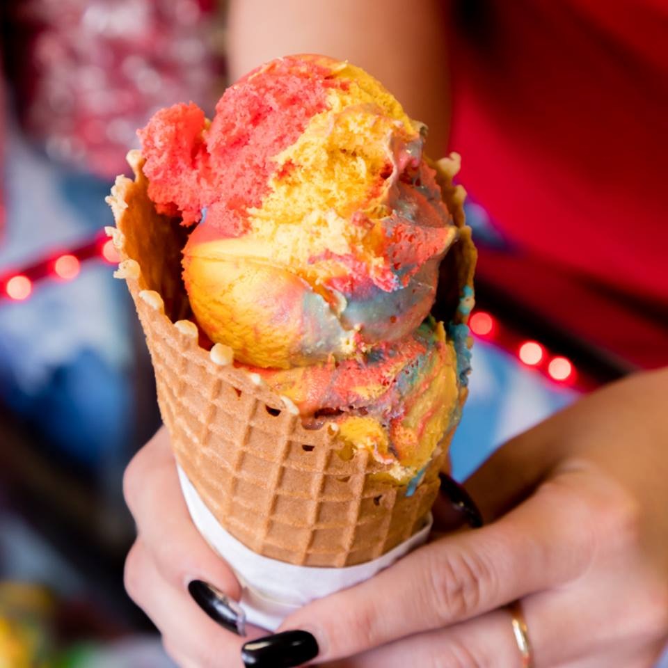 A hand holding a homemade waffle cone stacked with rainbow sherbet in the shop