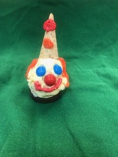 A clown face treat: ice cream on a cookie with an upturned cone hat, red nose and blue icing eyes