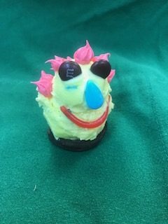 A party person treat on a cookie base, decorated with pink icing hair, candy sunglasses and a smile