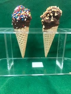 Two party cones dipped in chocolate — one rolled in rainbow sprinkles, one in chopped nuts